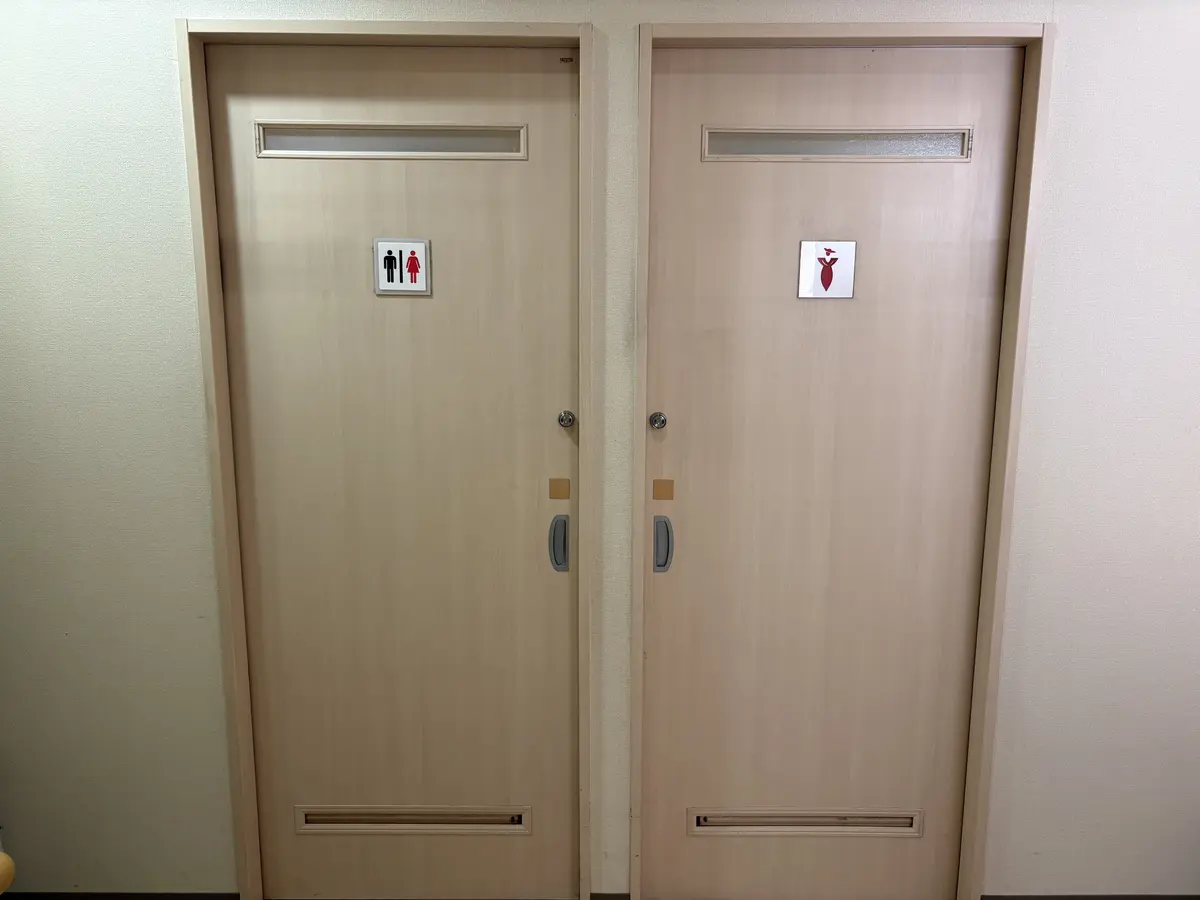 つつみ脳神経外科クリニックのお手洗い。木目調の扉が2つ並び、左は男女共用トイレ、右は女性専用トイレの案内表示がある。